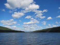 A body of water with hills and blue sky

Description automatically generated