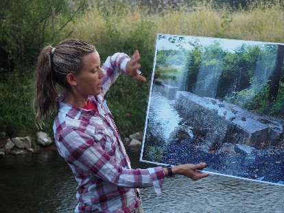 The image shows a person holding a photograph of a picturesque waterfall surrounded by a lush, green forest.
AI-generated content may be incorrect.