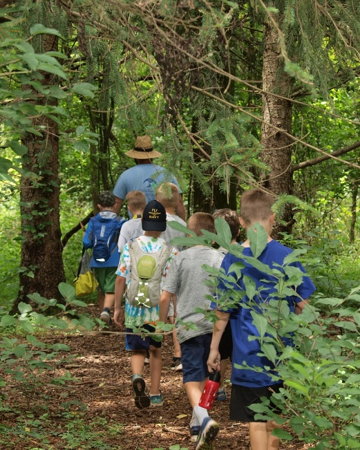 The image depicts a group of children, dressed in casual outdoor gear, walking down a forest trail amidst a lush, green environment.

AI-generated content may be incorrect.