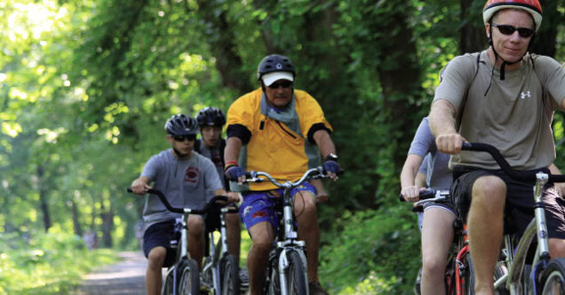 The image shows a group of people cycling along a tree-lined, shaded path.

AI-generated content may be incorrect.